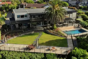 Aerial view of a premium Auckland home with swimming pool, multi-level decking, manicured lawn and mature landscaped gardens.
